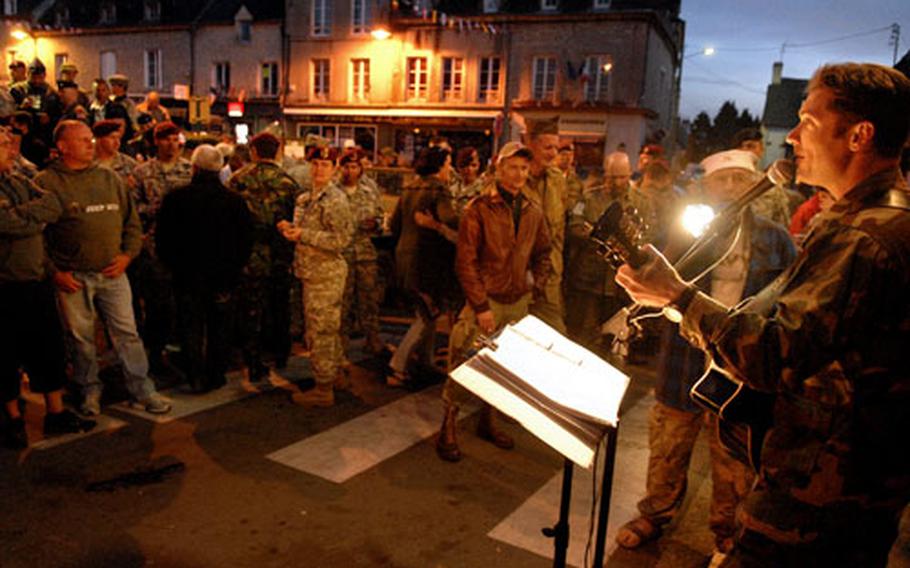 U.S. Navy Lt. Cmdr. Chris Irwin entertains veterans, reenactors, spectators and active-duty military from numerous countries Thursday on a crowded street in Sainte Mere Eglise, France.