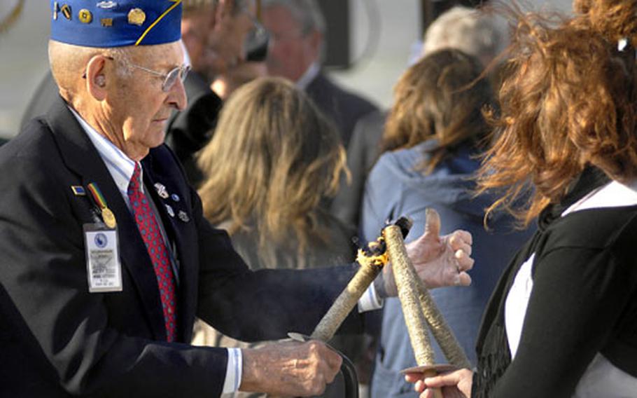 Arden Earll, a D-Day veteran from Erie, Pa, lights a torch during a ceremony Friday honoring National Guard soldiers near Omaha beach in Normandy, France.