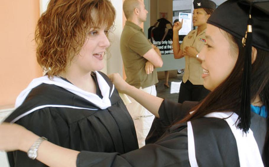 Suerjee Lee, right, makes sure Misty Owens&#39; gown and accessories are perfect before they head to their graduation ceremony, held Friday at the U.S. Navy Capodichino base. Both graduated from the University of Oklahoma with Masters degrees in human relations.