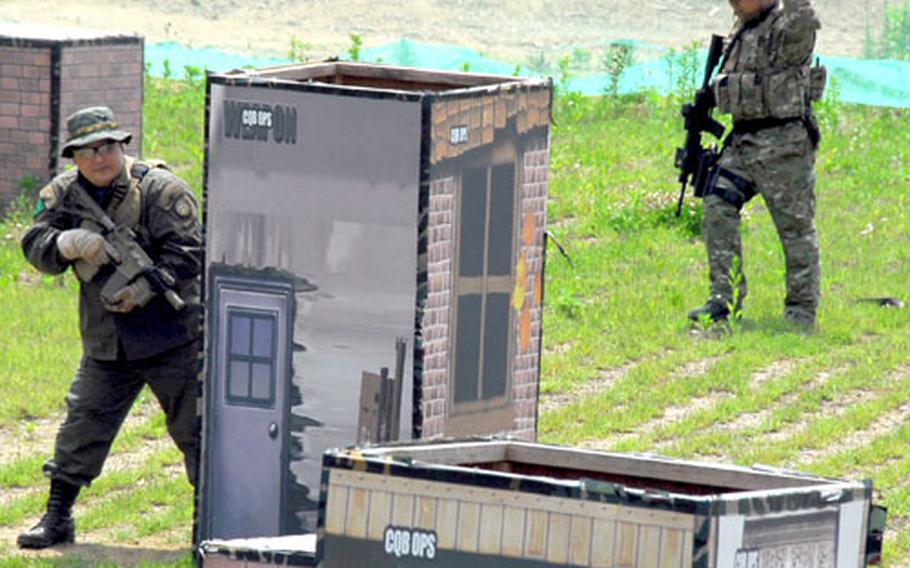 A man playing a survival game peers from behind a prop before taking a shot, while another man who has been shot raises his hand.