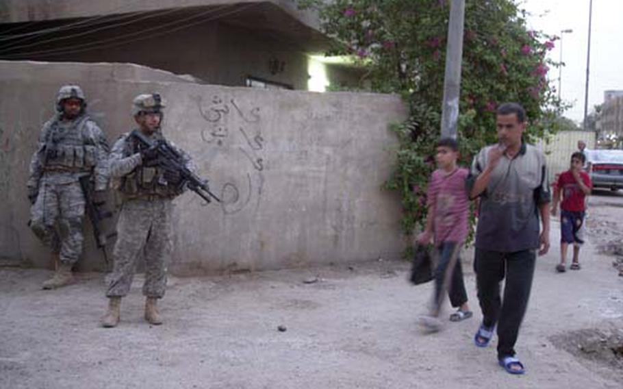 Two soldiers with Company C, 1st Battalion, 5th Cavalry Regiment look on as families walk through a neighborhood in Rusafa, part of eastern Baghdad. Company C is on a mission to find “rocket man,” the group of men who are shooting rockets into the Green Zone.