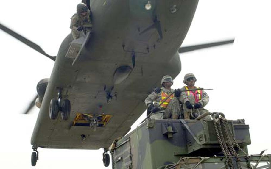 A member of a Chinook crew helps guide the helicopter down low enough so Pfc. Joseph Thames, Pfc. Leonard Ahmai and Staff Sgt. James Green can attach a vehicle to it.