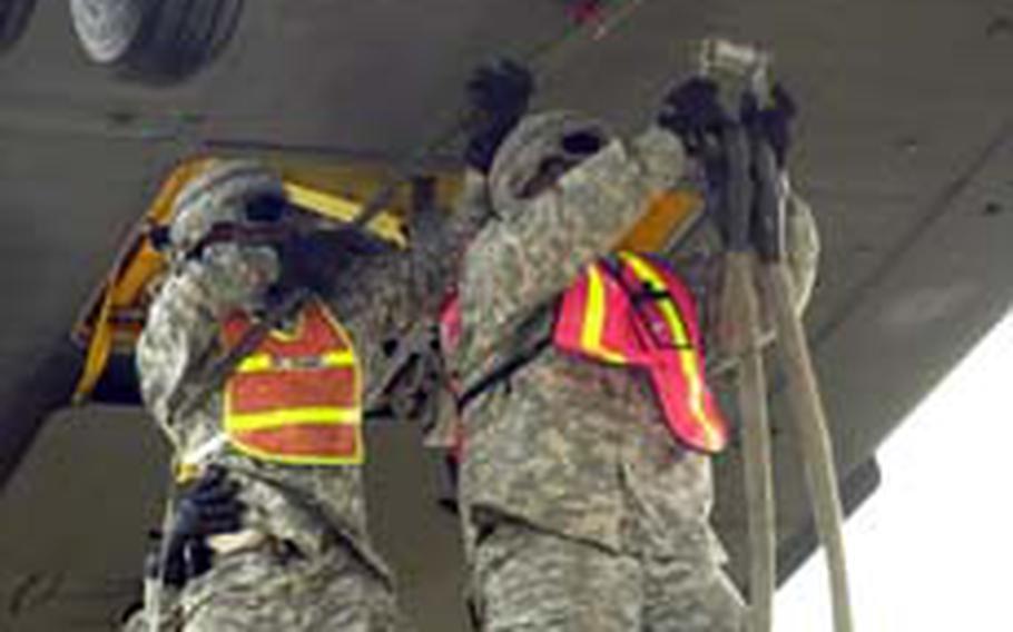 Pfc. Joseph Thames, left, hooks a ground rod to the underbelly of a Chinook hovering overhead as Pfc. Leonard Ahmai prepares to attach cables from a vehicle below to the helicopter during a sling-load training exercise Tuesday at Camp Mobile.