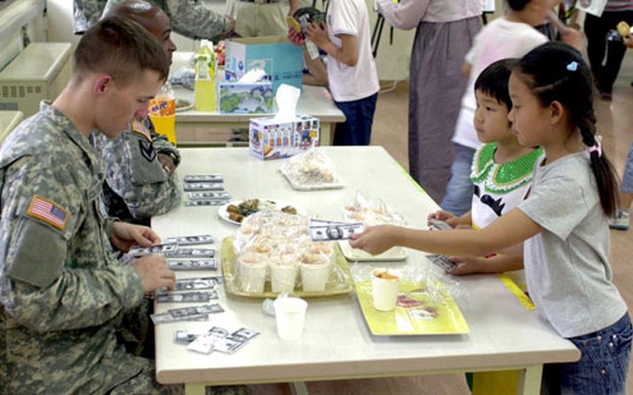 U.S. Army Lt. Dane Schoonover, left, sells treats to students at Daesungdong Elementary School during an "English market" Friday. Students learn the value of American money by spending fake bills on toys and treats.