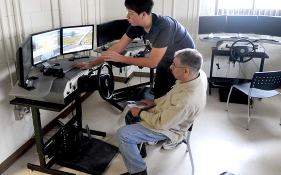 Stars and Stripes reporter Franklin Fisher, seated, is shown the workings of a high-tech driver training simulator that uses animated driving scenarios to help soldiers and others at Humphreys learn to drive or improve existing driving skills.