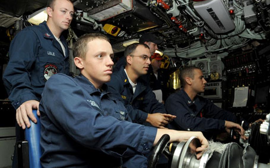 Seaman Dakota Bridgeman, foreground sitting, and Petty Officer 3rd Class Thayer McSwain steer the USS Seawolf following a dive near Okinawa May 3, with Petty Officer 3rd Class Andrew Lisle, left, and Ensign Ed Nixon observing. Bridgeman and McSwain are watching screens in front of them showing their depth, speed and other measurements. The Seawolf also drives in automatic mode in some situations.