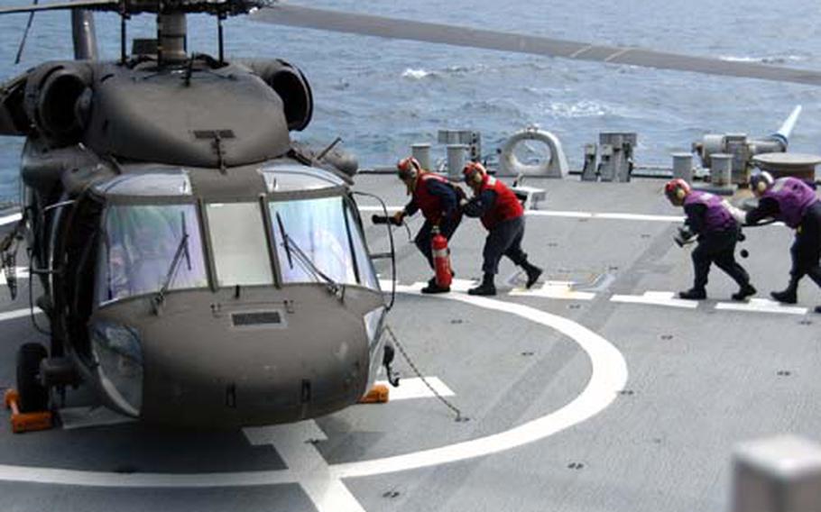 A USS Curtis Wilbur crew heads to a U.S. Army UH-60A helicopter to refuel it as Army pilots and crew qualify for shipboard certification Tuesday. The qualifications aboard the destroyer took place off the coast from Tokyo.