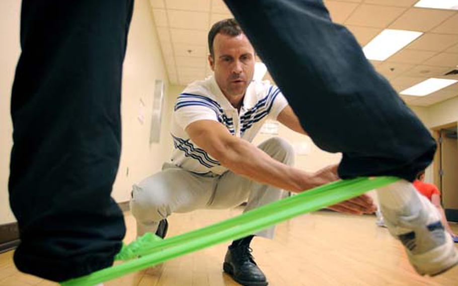 Franklin Fisher, foreground, executes a thigh-strengthening exercise using a 3-dimensional resistance band.
