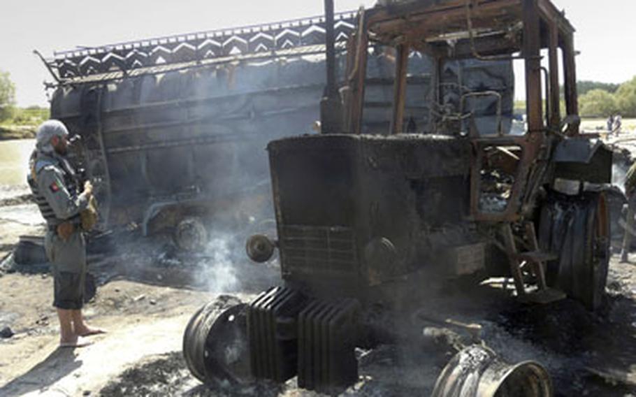 An Afghan security policeman, left, stands near a burnt fuel tanker and tractor in Kunduz, north of Kabul, Afghanistan, Friday. NATO jet blasted two fuel tankers hijacked by the Taliban in northern Afghanistan, setting off a huge fireball Friday that killed up to 90 people, Afghan officials said.