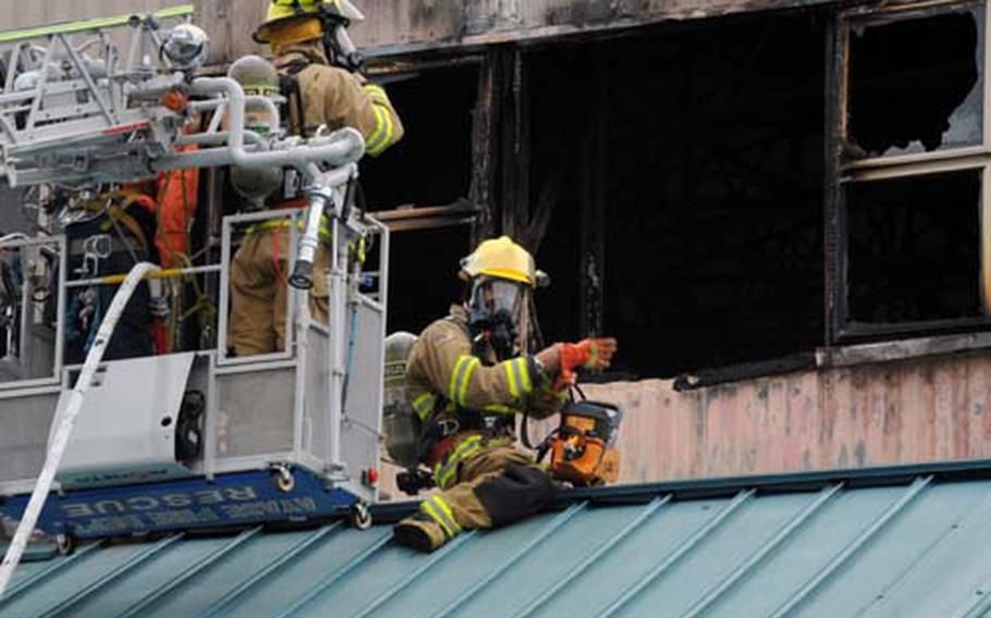 A Naval Air Facility Atsugi, Japan, firefighter prepares to cut a hole in the roof of Hangar 183 on Saturday after a fire there was suppressed. The fire was reported about 11:45 a.m., and fire departments from the air facility and Yamato and Ayase cities responded. Officials said three people were injured.
