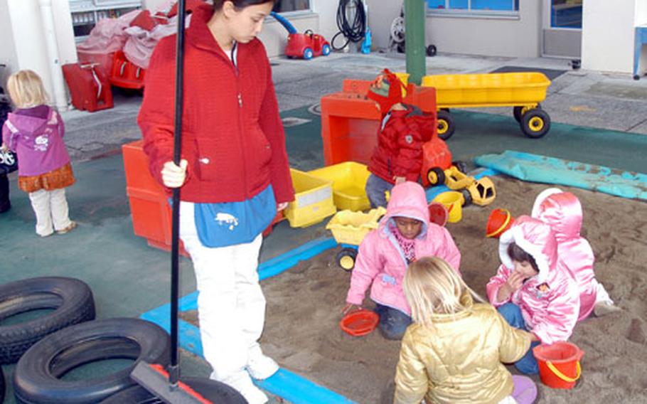 Erin Becote, a teacher in the preschool room at Yokosuka Naval Base's Child Development Center, talks with children as they play in the center's sandbox.
