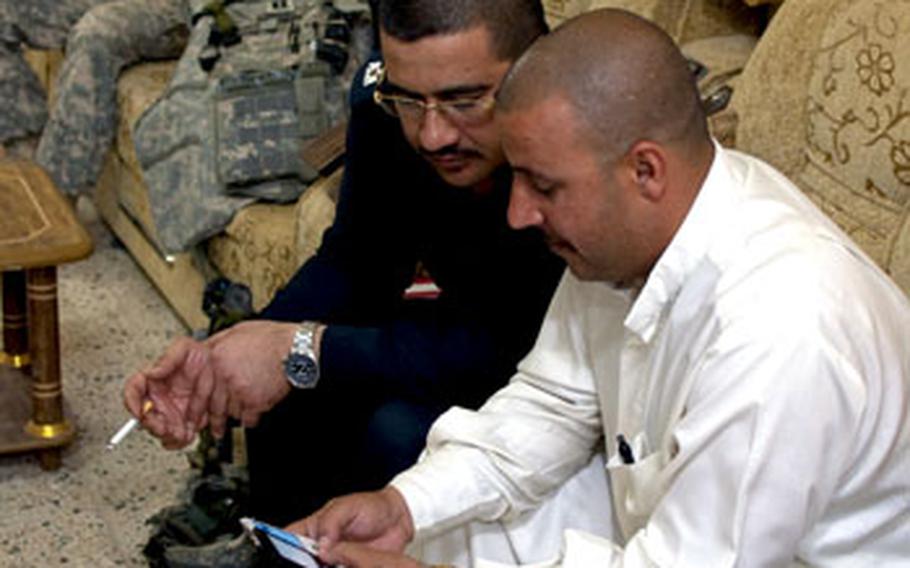 Iraqi police Sgt. Maj. Jassim Mohammed Ali al-Tikriti, right, and Major Bashar Fouad Younis Mohammed look at images on a cell phone as they plan a raid in Hawijah. U.S. Army Staff Sgt. James Davis waits in the background.