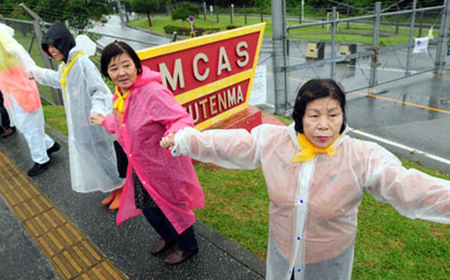 A few of the thousands of anti-base protesters at Marine Corps Air Station Futenma hold hands Sunday in front of the base sign. The organizers of the event claimed success on two of three attempts to join hands around the eight-mile fence line, symbolically closing the controversial base.