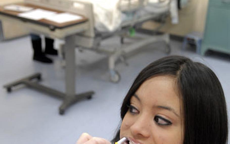 Rachele Hernandez gets her teeth brushed by Samantha Brown as part of health science class in January at Ramstein High School. Students experience a wide range of nursing skills such as changing sheets with a patient still in the bed, seen in the background, during the course with an opportunity to become certified as a nursing aidd after working at Landstuhl Regional Medical Center.