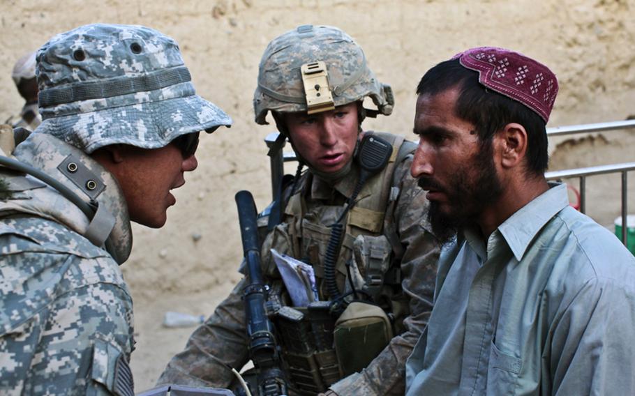 As Staff Sgt. Erik Adams, a soldier with Company B, 2nd Battalion, 508th Parachute Infantry Regiment, looks on, an interpreter questions a man about opium seed, a bag of spent AK-47 bullet casings and banned ammonium nitrate fertilizer found in his compound in the village of Deh-e-Kuchay, in the Arghandab valley of southern Afghanistan's Kandahar province. May 22, 2010.