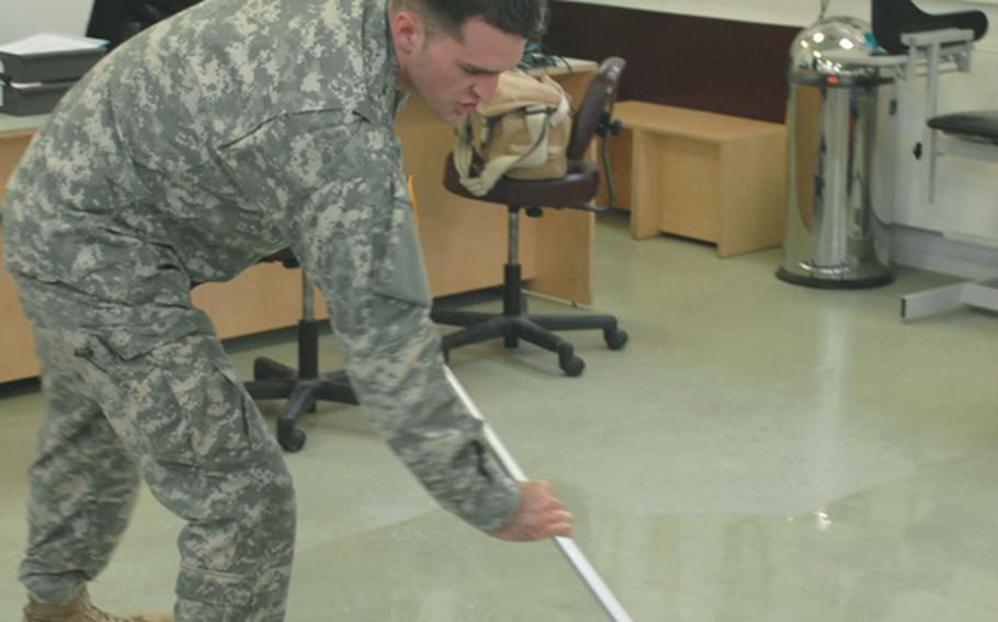 Spc. Joshua Sandlin with the Wiesbaden Soldier Medical Readiness Center in Wiesbaden, Germany, takes time from helping customers to mop the office floors Thursday. Installation Management Command-Europe is hoping to save $2 million annually by eliminating cleaning contracts for units that are smaller than a brigade.