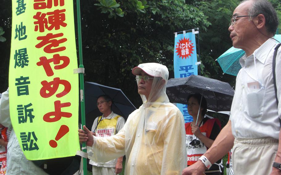 Eisho Nakandakari, center, from Ginowan, Okinawa, stands among about 200 residents and supporters Thursday outside the Fukuoka High Court branch in Naha. The banner he holds demands a stop to flight operations at Marine Corps Air Station Futenma in Ginowan.