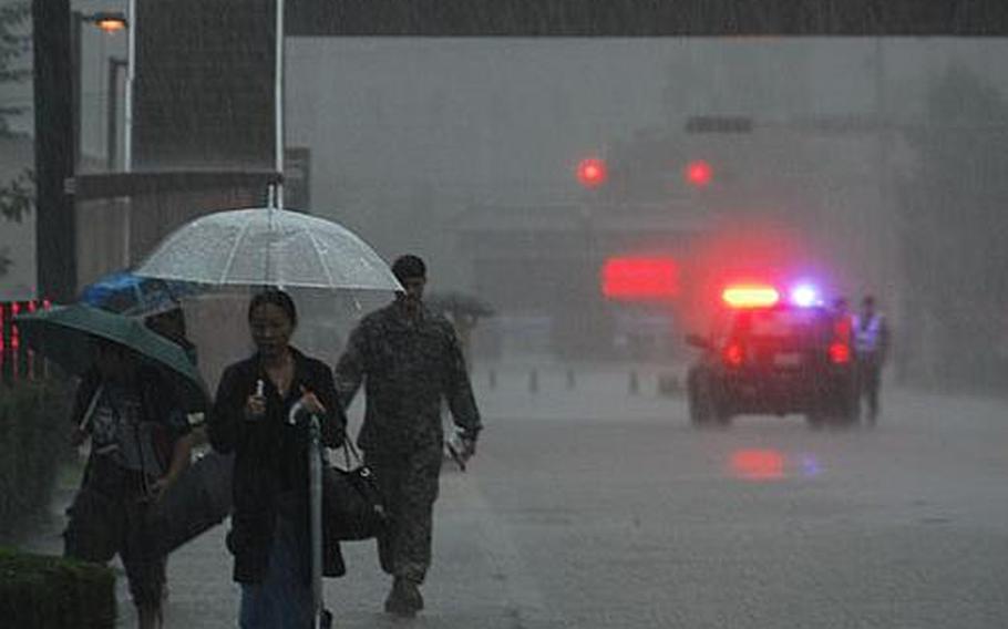 A police car blocks traffic on 8th Army Drive on Tuesday afternoon as children leave school. Portions of the road, as well as other low-lying areas at U.S. Army Garrison-Yongsan, were closed Tuesday due to flash flooding.
