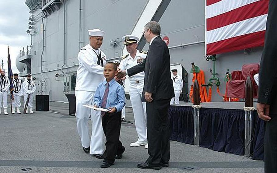 Trinol Von Mondaya, 7, walks away with his certificate after being greeted by USS Essex commander Capt. David Fluker and Kenneth Sherman, from the U.S. Citizenship and Immigration Services. The boy is followed by his father, USS Germantown Petty Officer 1st Class Trinol Mondaya.
