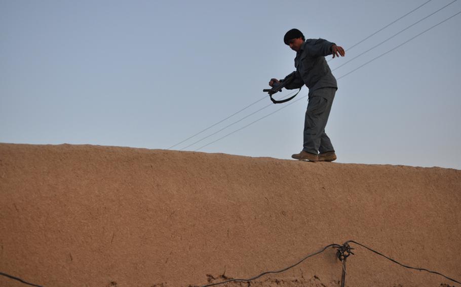 An Afghan policeman walks along a compound wall during a raid in Kandahar City.