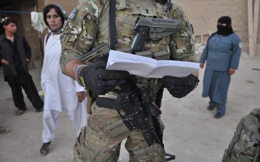 First Lt. Lee Robinson, of Apache Troop, 1-10 Cavalry, checked his maps during ''soft-knock'' raid in mid-September in Kandahar City. Behind him, female Afghan security officers search the compound.