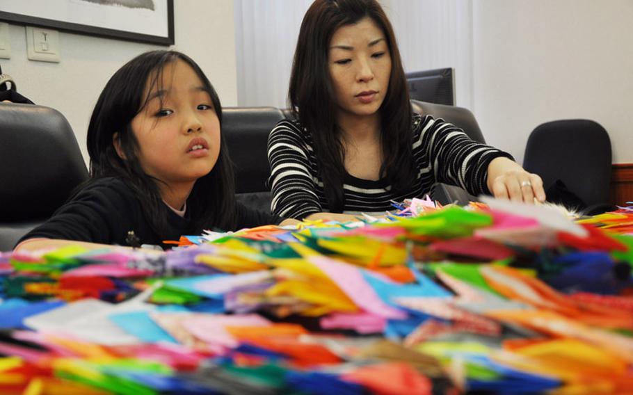 Fukushima evacuees Rico Osawa, and her mother, Shoko Osawa, attend a ceremony presenting U.S. Navy sailors with strings of paper cranes at Yokosuka Naval Base in February. Japanese citizens and others belonging to the military spouse-led Helping Hands for Tohoku charity group made the cranes. Japanese citizens and disaster survivors also wrote personal thank-you notes to the sailors who provided aid during the disaster.