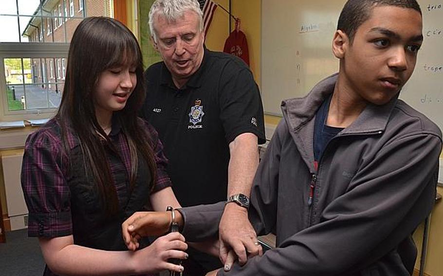 Victoria Littlejohn, an eighth grader at Lakenheath Middle School, handcuffs classmate Elijah Miller under the direction of Paul Glover, police constable, as part of a presentation about English police during UK Day events at RAF Feltwell on May 3, 2013. Glover taught the students tactics for handcuffing suspects, including forcing the suspect to look away so it is harder for the person being handcuffed to fight.