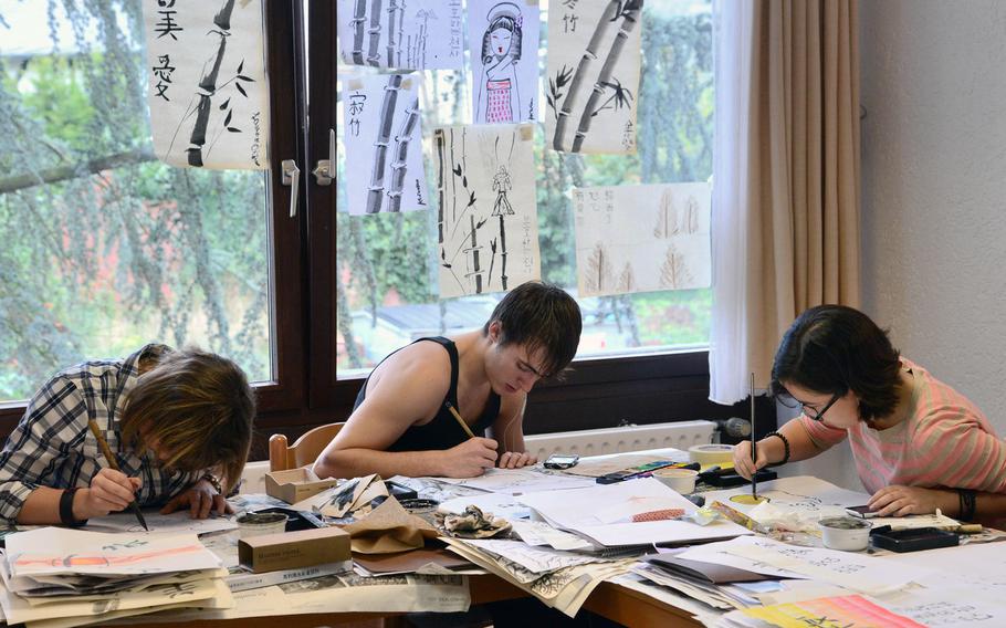 In the calligraphy workshop at Creative Connections, Vicenza's Alexandra Bass, Aviano's Levi Robertson and Lauren O'Brien of Naples work on their pieces. Finished works hang on the window behind them. More than 160 students from DODDS-Europe high schools participated in this year's event that features 11 workshops in the visual and performing arts.