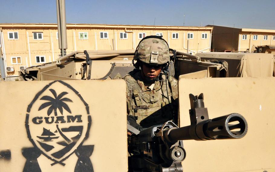 Spc. Joshua Babauta, a gunner with Headquarters Company, 1st Battalion, 294th Infantry Regiment, loads his gun atop a MRAP in preparation for a security escort mission in Kabul. The logo painted on the gun's side shield is in the shape of a sling stone, representing the warrior culture of Guam's Chamorro people.