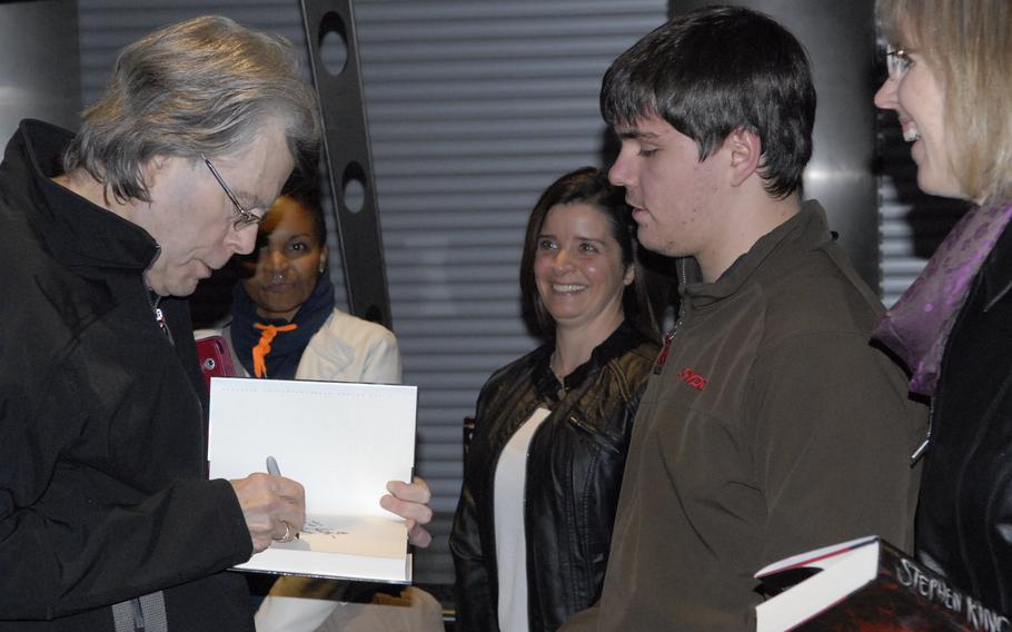 Stephen King, American author of contemporary horror, suspense, science fiction and fantasy, signs a copy of his new book, "Doctor Sleep," for Andrew Bolton and his mom, Laura, right, prior to his book reading at Ramstein Air Base, Germany, on Monday, Nov. 18, 2013. The Boltons won tickets to the limited-seating event in an American Forces Network contest.