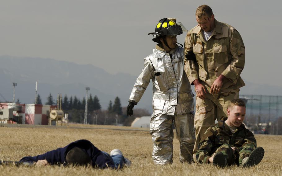 A firefighter from the Yokota Fire Department escorts an air crewman assigned to the 374th Airlift from the scene of a simulated C-130 Hercules crash at Yokota Air Base March 3, 2014 during the Samurai Readiness Inspection.