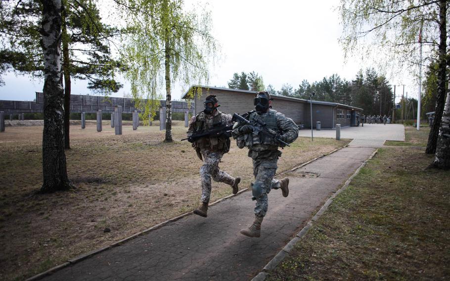 An American and a Latvian soldier sprint in full gear and gas masks at the start of a stress shooting competition on Wednesday, April 30, 2014, meant to build camaraderie and test their endurance and marksmanship under simulated battlefield conditions.