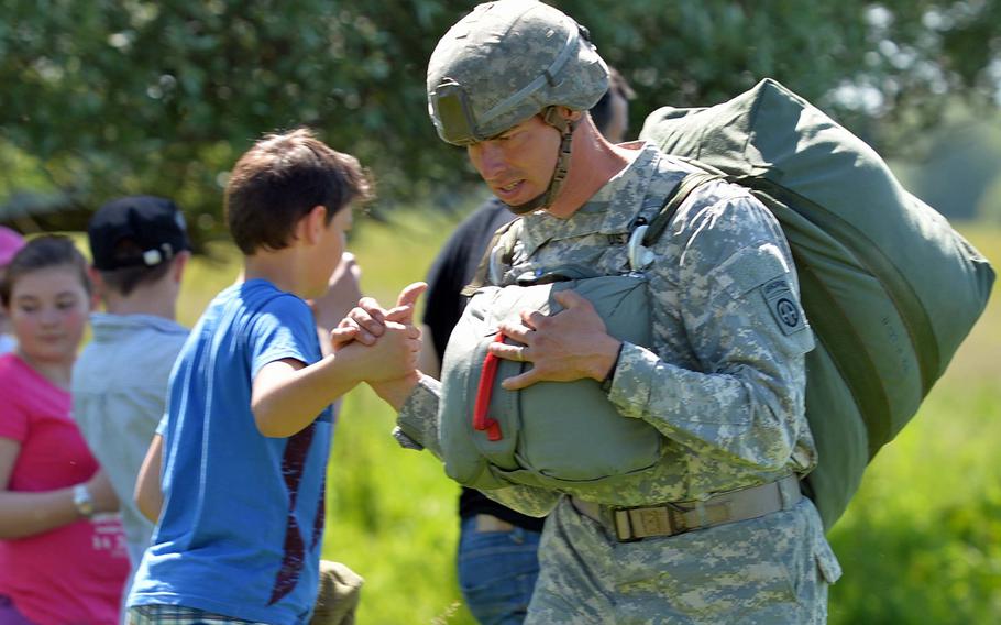 Staff Sgt. Bruce Nelson of the 82nd Airborne Division shakes hands with a French boy after parachuting into La Fi??re drop zone near Cauquigny, France, Sunday, June 8, 2014, in a 70th anniversary of D-Day commemoration.