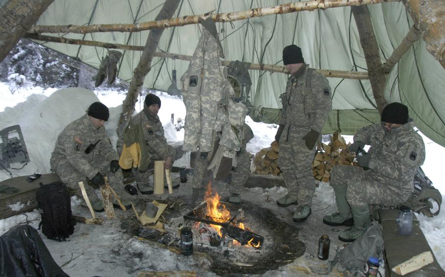 Army aviators stay warm during Arctic survival training in Alaska on Feb. 10, 2015. The soldiers huddled together for warmth around a large, comforting blaze under a parachute that kept snow flurries from their heads. Seth Robson/Stars and Stripes