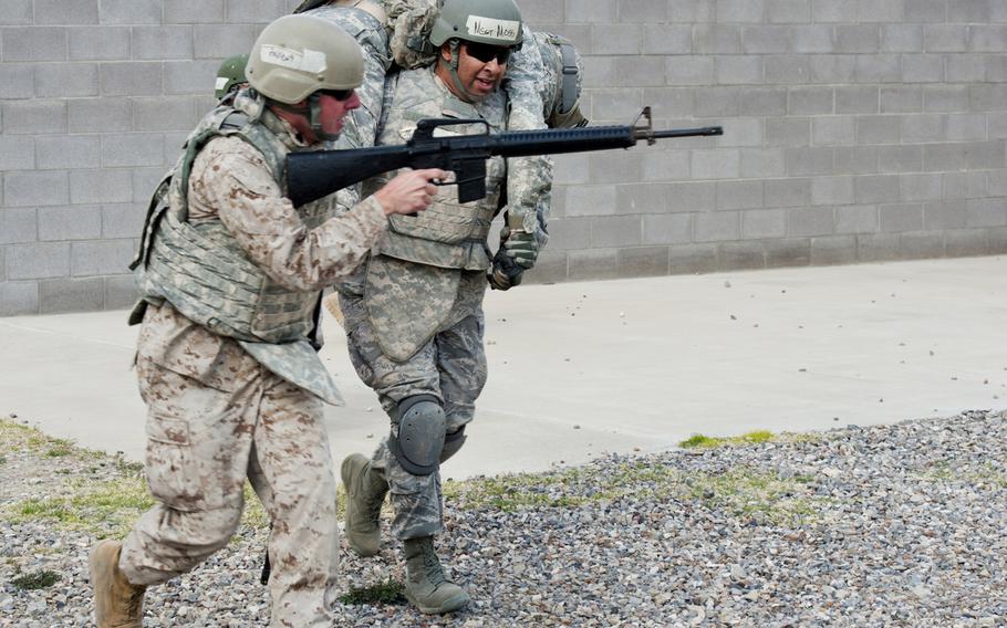 U.S. Army Sgt. 1st Class Matthew Girad is carried by U.S. Air Force Master Sgt. Eric Moss, while U.S. Marine Sgt. Trevor Andrews provides cover during small unit tactics training at Fort Bliss, Texas, on March 14, 2015, as part of Operational Contract Support Joint Exercise 2015.