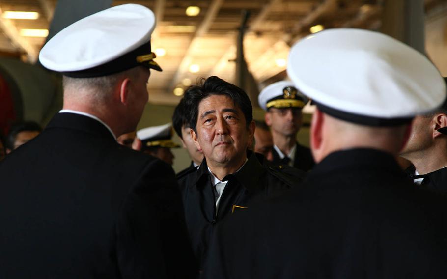 Japanese Prime Minister Shinzo Abe, center, listens as Capt. Christopher Bolt, left, commanding officer of the aircraft carrier USS Ronald Reagan, and Rear Adm. John Alexander, commander of Battle Force 7th Fleet, explain shipboard operations duirng a tour of the ship's hangar bay, Oct. 18, 2015. Abe defended the necessity of his nation's security alliance with the United States and spoke out Tuesday against "naked nationalism" amid the U.S. presidential campaign's often contentious rhetoric.