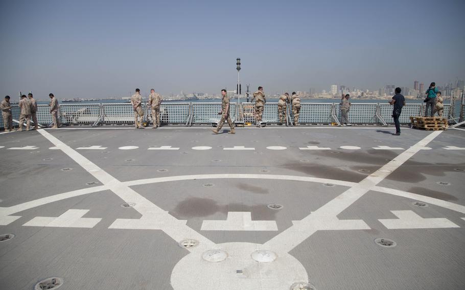 Personnel and media from several nations stand on the flight deck, watch and take pictures as the auxiliary expeditionary fast transport ship USNS Choctaw County leaves port in Bahrain during the International Mine Countermeasures Exercise on April 10, 2016.