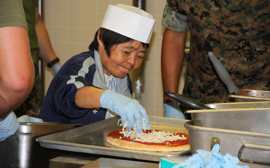 A resident from the Reimei No Sato home for disabled adults in Uruma puts cheese on her pizza during a ''Make your own pizza,'' event at the 12th Marines Mess Hall on Camp Hansen on Thursday, July 7, 2016. The event is one of half a dozen exchanges between the Marines and residents from the home held each year.