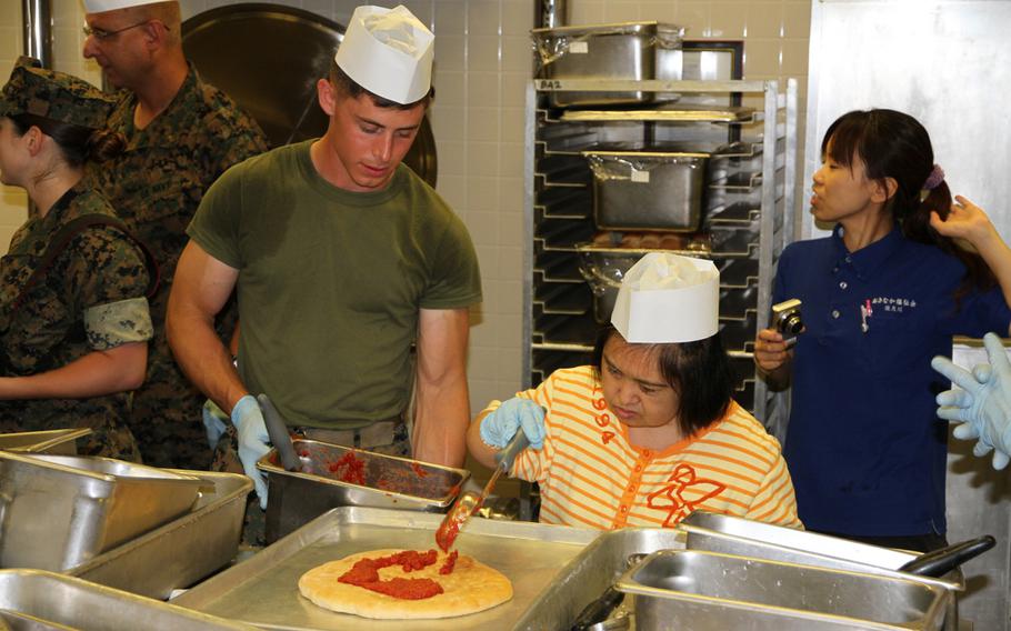 Marine Lance Cpl. Kyle Campbell, left, helps a resident from Reimei No Sato home for disabled adults sauce a pizza during a ''Make your own pizza,'' exchange event on Thursday, July 7, 2016, at Camp Hansen.