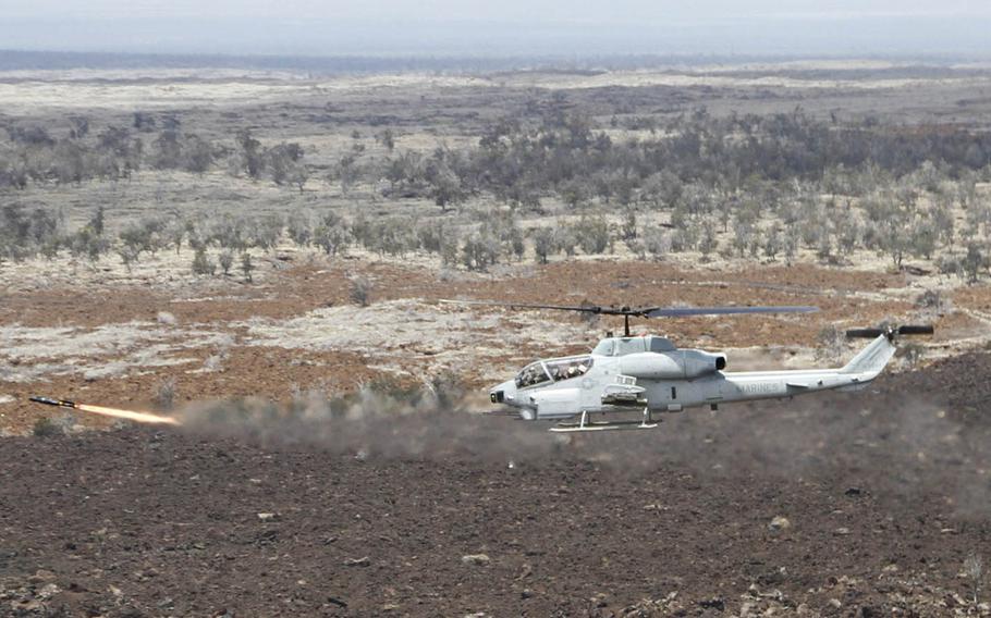 As viewed from the adjacent Huey, a Cobra attack helicopter fires a Hellfire missile at a target on the live-fire range of the Pohakuloa Training Area, Hawaii, July 20, 2016.