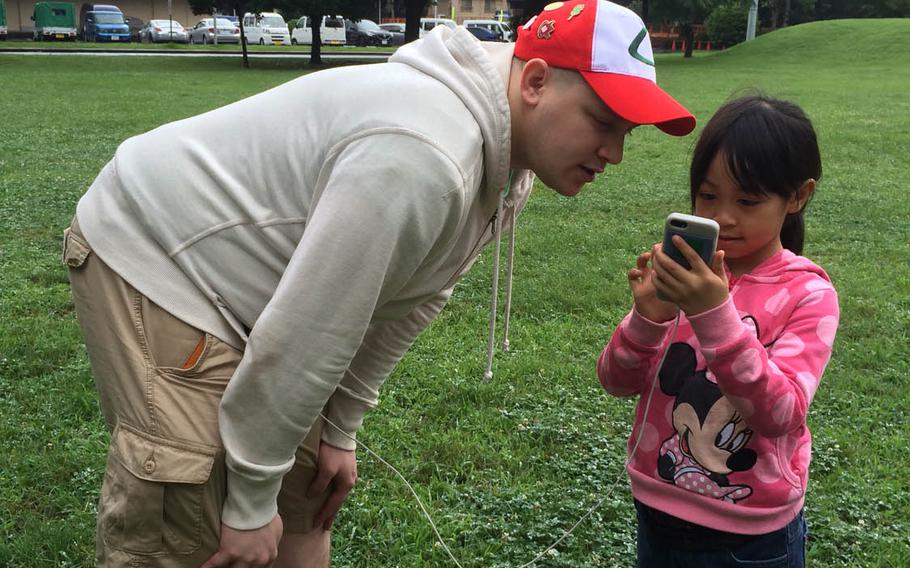 Air Force Staff Sgt. Richard Mahoney, 29, of Geneva, N.Y., hunts for Pokemon with his daughter, Julian, 6, at Yokota Air Base, Japan, Friday, July 22, 2016. The popular Pokemon Go augmented-reality game went live in Japan on Friday.