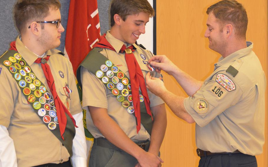 John Brandt, assistant scoutmaster for Boy Scout Troop 106 in Wiesbaden, Germany, pins the Eagle Scout badge on Adam Cloud of Wiesbaden, as fellow Eagle Scout badge recipient Michael Brandt, also of Wiesbaden, looks on, Sunday, Sept. 25, 2016.