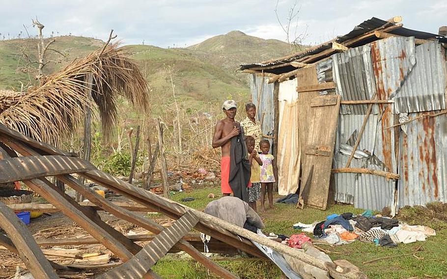 A family in the southwest Haiti village of Jabouin stands on Oct. 18 between their destroyed home to the left and the makeshift shack they cobbled together after Hurricane Matthew left the without shelter. 