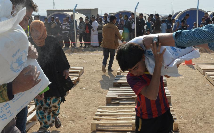 A man loads bags of dry food on the shoulders of a young boy during the distribution of family rations at a displacement camp in Hassan Sham, Iraq, on Monday, Nov. 7, 2016. Families began arriving at the camp as Iraqi forces pushed into Mosul's suburbs and outer neighborhoods during the operation to oust the Islamic State group, which has controlled the area for more than two years.