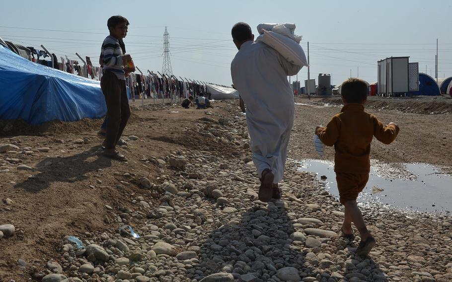 A boy follows his father as the man carries the family's monthly food ration to the quonset hut shelter where they were staying at a displacement camp in Hassan Sham, Iraq, on Monday, Nov. 7, 2016.