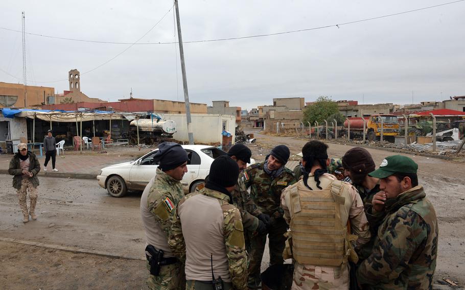 Nineveh Plain Protection Units fighters warm their hands at a barrel fire near a command post for the Christian militia in Qaraqosh, Iraq, on Saturday, Dec.17, 2016.