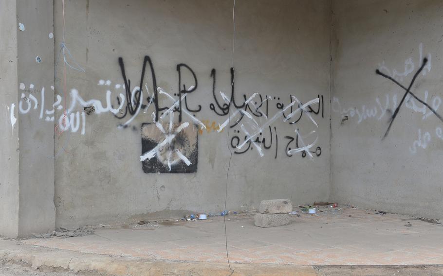 An Islamic State group flag painted on the wall of a building in Qaraqosh, Iraq, on Saturday, Dec. 17, 2016, is painted over with the initials of the Nineveh Plain Protection Units, an Assyrian Christian militia.