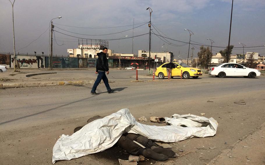 Traffic passes the body of a person locals said was an Islamic State fighter, near Mosul University on Saturday, Jan. 21, 2017. 