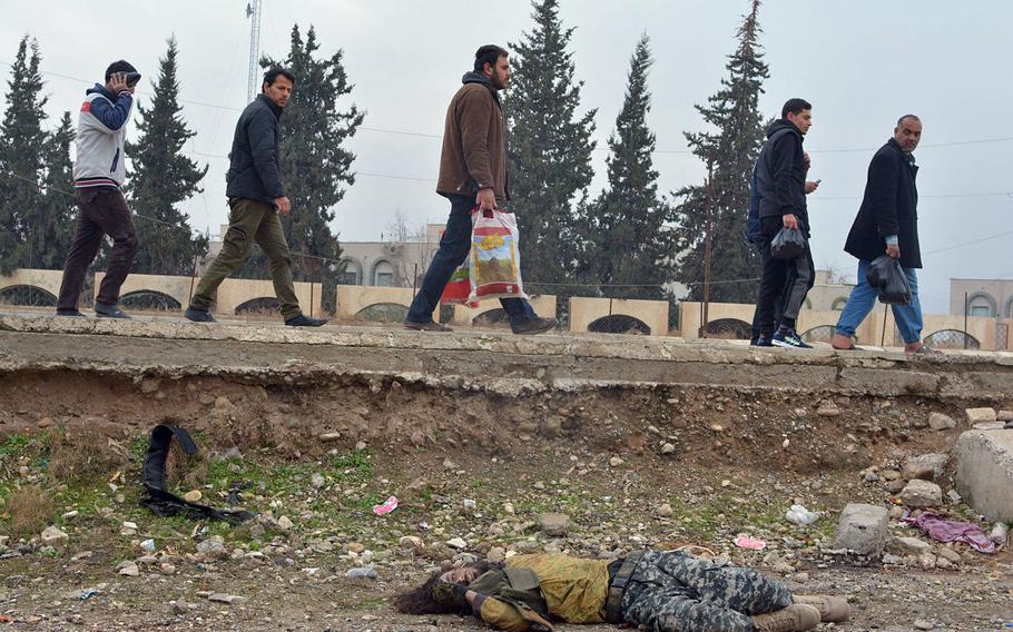 Residents pass a dead Islamic State fighter in Mosul's al-Arabi neighborhood on Wednesday, Jan. 25, 2017. What appears to be a suicide bomb vest lies near the body.
