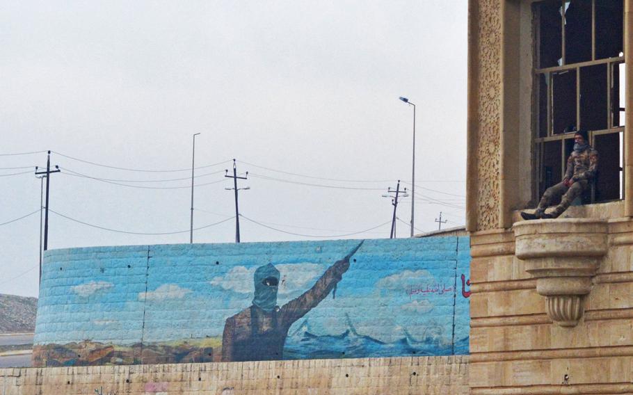 An Iraqi soldier sits in a palace window in Mosul on Wednesday, Jan. 25, 2017. The Islamic State mural behind him depicts the group's dream of the conquest of Rome.